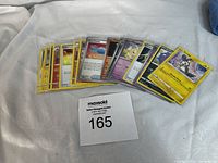 Wide view of the lot of approximately 20 used Pokémon cards laid out on white cloth showing a variety of Pokémon characters and energy cards.
