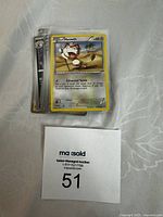 Stack of Pokémon cards with Meowth card visible on top and auction lot card labeled 51.