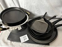 Lot of pots, pans, and microwave dish arranged on black surface, showing multiple pans stacked and the pot with handles and microwave dish on top.