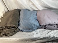 Three bundles of folded sheets in brown, light blue, and purple colors shown together on a white surface.