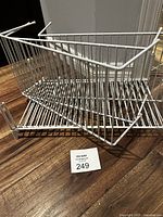 Two white metal wire shelves arranged with vertical dividers and hooks for cabinet installation.