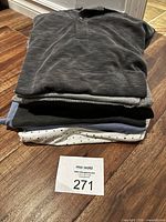 Stack of five folded shirts including dark grey textured pullover and patterned white shirt