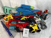 Photo showing the full lot from above, includes multiple toy blasters and assorted toys with a note number 23.