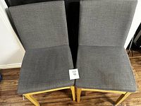 Two grey fabric chairs with light wooden legs side by side on wooden floor.