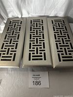 Three similar metal vent covers laid side by side, showing geometric rectangular cutout patterns and worn painted finish.