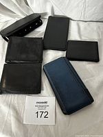 Five wallets arranged on white fabric background showing condition and style of each wallet