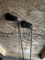 Photo showing the two clubs standing upright with their covers placed on the heads, against a plywood background.