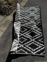Photo showing the outdoor carpet partially rolled with visible geometric diamond black and white pattern