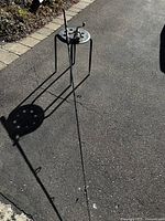 Fishing rod leaning against the black metal outdoor table on pavement, showing overall view and size