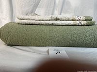 Side view stack of folded queen quilt with pillow shams on top showing thickness and olive green color