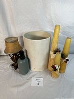 Photo showing soap dispenser, lamp-style candle holder with shade, three decorated Christmas candles, and white garbage can.