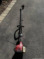 Full view of the gasoline powered string mower lying on pavement, showing long shaft and red motor housing.