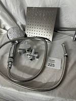 Photo showing the large square rain shower head with water outlet holes, round handheld shower head connected to flexible metal hose, valve fitting, and wall mount holder.
