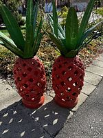 Two large red lattice pineapples with green leaves outdoors on a stone pathway