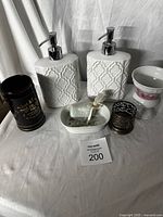 Full lot showing two white ceramic soap dispensers with raised geometric pattern, toothbrush holders, soap holder with soap, and small decorative metal holder.