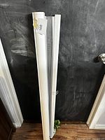 Full view of white roller window shade leaning against a dark wall, showing approximate length and condition.