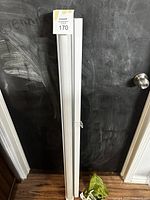 White roller window shade rolled up, showing the full length and housing with pull chain.