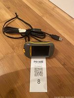 Garmin Dakota 10 handheld GPS device with attached USB cable on wooden surface.