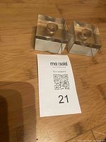Two clear resin cube candleholders shown on a wood surface alongside a MaxSold lot number card.