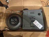 Photo showing Kodak Carousel S slide projector and Kodak circular slide carousel tray in cardboard box.