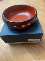 Top angle photo of the circular lacquer bowl with glossy black exterior and red interior with yellow diamond motifs on the exterior.