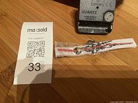 Top down photo of the clock mechanism motor and clock hands in plastic packaging, alongside a MaxSold auction lot card.