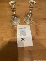 Pair of sterling silver candlesticks on wooden floor with MaxSold tag