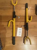 Two yellow steering wheel locks laid on a wooden floor, one with 2 keys and the other with 1 key attached to their locking mechanisms.