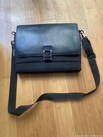 Front view of the closed black leather and fabric messenger bag with adjustable shoulder strap.