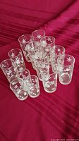 Group of 13 clear glasses with white snowflake patterns in 4 different sizes arranged on red cloth