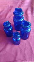 Set of four cobalt blue glass jars with lids arranged on red fabric background