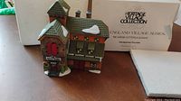 Front view of Dept 56 England Village Series McGree Cutters & Sleighs building with packaging visible in the background.