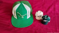 Green and white vintage Philadelphia Eagles trucker cap alongside salt and pepper shakers shaped like Eagles jerseys on red fabric background.