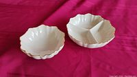 Two Lenox white porcelain serving bowls on red fabric background, one bowl divided into three compartments with scalloped edges and gold trim.