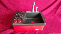 Plastic Little Tikes kitchen playset sink unit with faucet and two stove burners visible, large basin sink with red drain plug