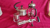 Wide view of four kitchen items on red cloth: MCM teapot, Bodum French press, stainless steel butter keeper, and chrome flint egg beaters.