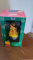 Photo of the figurine inside the original green box with snowflake decorations and Pooh graphics.