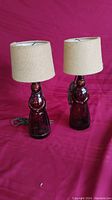 Pair of Mrs. Butterworth glass bottle lamps with beige fabric shades on a red background.