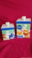 Two Pillsbury Doughboy ceramic canisters from Danbury Mint, tea canister (6" square) and sugar canister (6"x7"), front side show Doughboy and themed graphics with lids topped with chef hat-shaped handles.