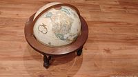 Top view showing cream-colored globe with detailed vintage-style map, mounted on a round wooden frame atop three wooden legs.