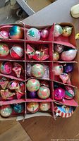 Overview of tray lot showing divided cardboard packaging filled with assorted vintage glass Christmas ornaments in various colors and shapes.