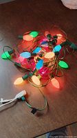 A tangled string of vintage large bulb Christmas lights with various colors glowing on a brown wooden surface.