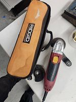 Ridgid corded multi tool with power cord and yellow switch, next to tan Ridgid branded carrying case with stains