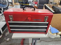 Photo of closed red Craftsman tool box with handle, lock, and latches on a white table.