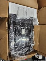 Photo of the whole body vibration platform wrapped in plastic inside a cardboard box with instruction manual visible.