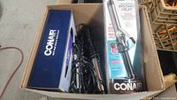 Box containing multiple Conair hair styling tools including a hair dryer and curling irons with cords visible.