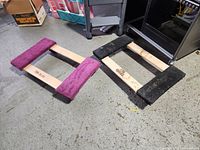 Both wooden furniture dollies shown side by side on concrete floor, one with black carpet pads and the other with purple carpet pads.