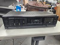 Front view of Kenwood AM-FM stereo receiver showing analog tuning and control panel including power, speaker switches and sliders for bass, treble, balance.