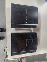 Top view of two black Sony PlayStation 3 consoles showing surface scratches and scuffs.