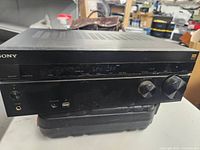 Front view of Sony AV receiver showing power button, headphone jack, digital display, input selector, and volume knobs.